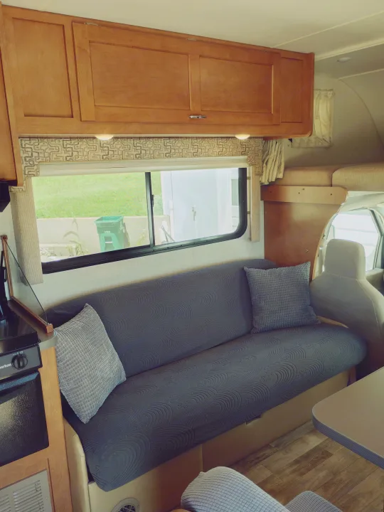 Cozy RV rental interior with a gray sofa, wooden cabinets, and kitchen area, offering comfort for your travels.. Winnebago Minnie Winnie 2017