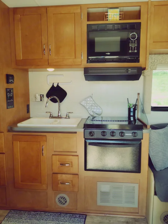 Compact and organized RV rental kitchen featuring light wood cabinetry, microwave, stove/oven, and sink.. Winnebago Minnie Winnie 2017