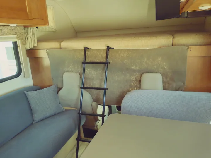 Cozy RV rental interior showing a bunk bed with ladder, blue couch, and dining table. Perfect for family travel.. Winnebago Minnie Winnie 2017