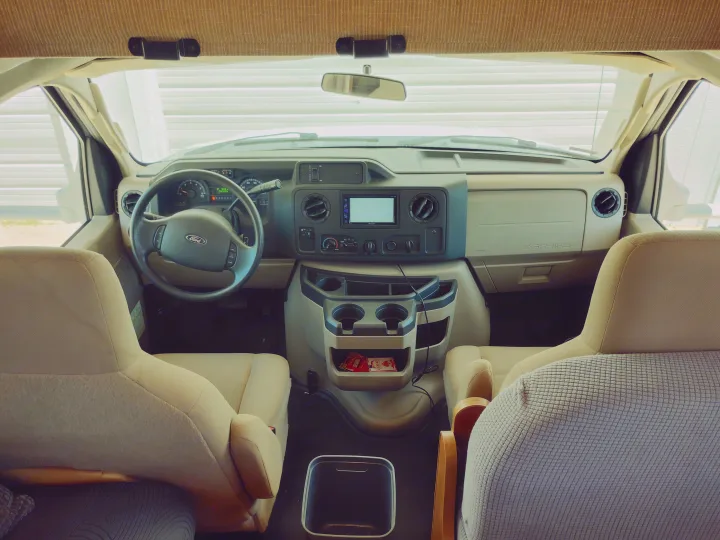RV rental cockpit view from the rear, showing the Ford steering wheel, dashboard, center console, and front seats.. Winnebago Minnie Winnie 2017