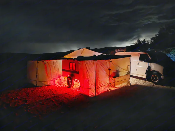 RV rental night setup: small trailer, van, and illuminated awnings with red lights under cloudy skies, perfect for camping.. Runaway Cool Camp 4x8 2018