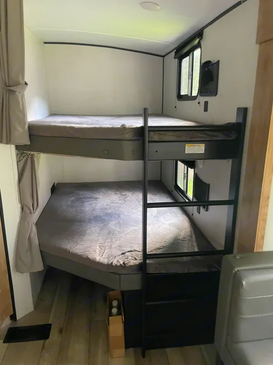RV rental with stacked bunk beds, gray mattresses, and windows. This cozy interior offers a comfortable sleeping arrangement.. Keystone RV Springdale 2022
