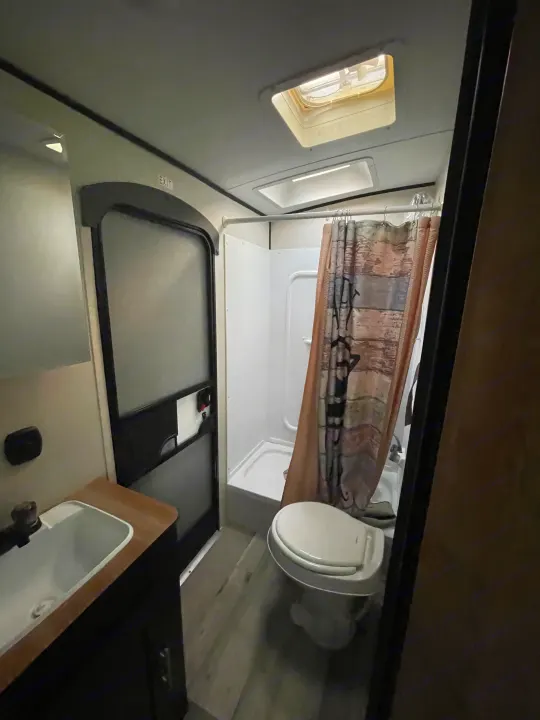 RV rental bathroom featuring a compact sink, toilet, shower with curtain, skylights, and an "EXIT" sign above the door.. Keystone RV Springdale 2022