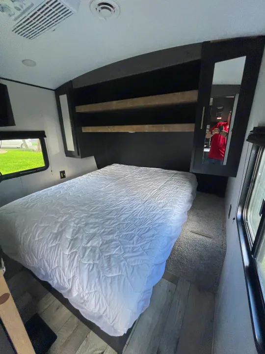 RV rental bedroom: cozy space with a large bed, overhead storage, and natural light from windows.. Keystone RV Springdale 2022