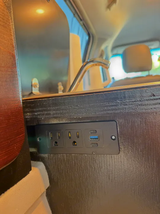 RV rental interior with embedded power strip: two AC, one USB-A, and two USB-C ports in dark wood paneling.. Chrysler Town & County 2010