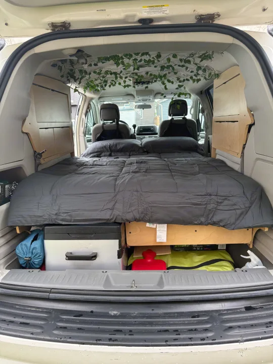 Minivan camper conversion for an RV rental, featuring a comfortable bed, under-bed storage, custom panels, and ivy decor.. Volkswagen Routan 2011