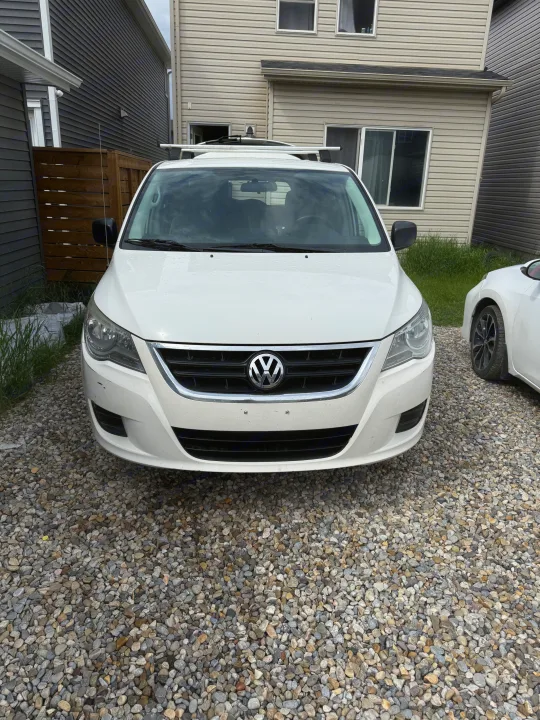 Front view of a white Volkswagen Routan minivan with roof rack on gravel, parked between houses, suitable for RV rental travel.. Volkswagen Routan 2011
