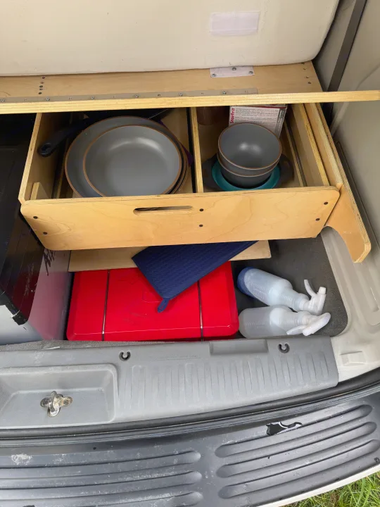 Inside an RV rental: a compact, organized camp kitchen with a wooden drawer holding dishes, a portable stove, and cleaning supplies.. Volkswagen Routan 2011