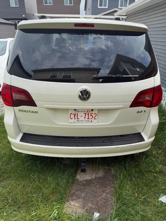 White Volkswagen Routan minivan (CYL-7152) rear, parked on grass with a tow hitch. A versatile option for an RV rental adventure.. Volkswagen Routan 2011