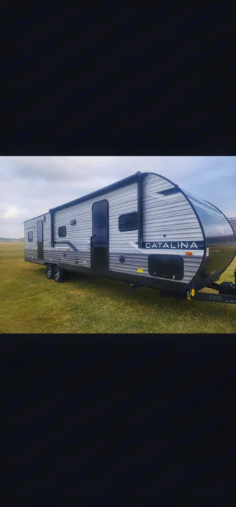 This grey and black Catalina travel trailer RV, parked on a grassy field under an overcast sky, is ideal for an rv rental.. Coachmen 29THS 2025
