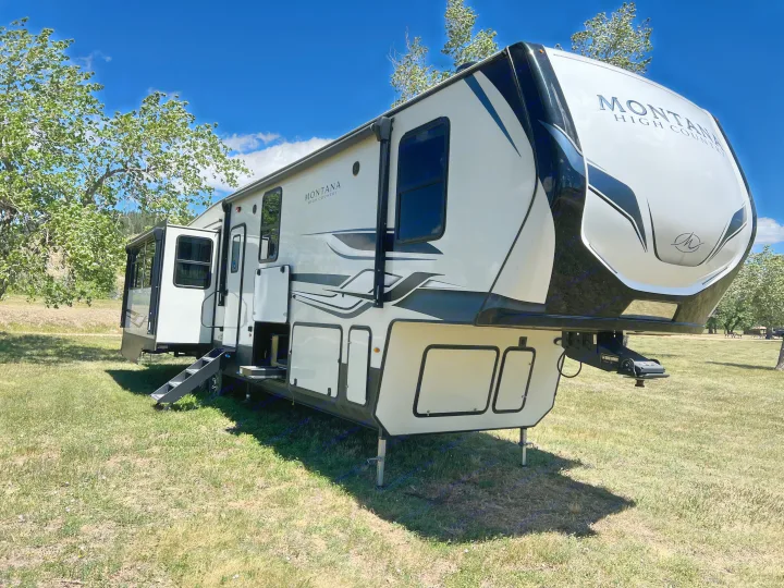 RV rental: A Montana High Country fifth-wheel RV is set up on a grassy site with slide-outs extended, ready for a camping trip.. Keystone RV Montana 2022