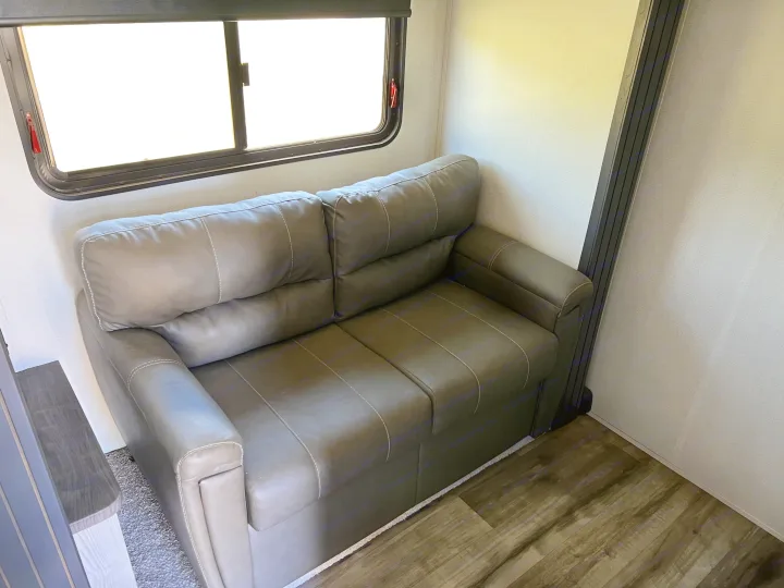 Enjoy the comfort of this grey faux leather sofa and window in your rv rental, ideal for relaxing journeys.. Keystone RV Montana 2022