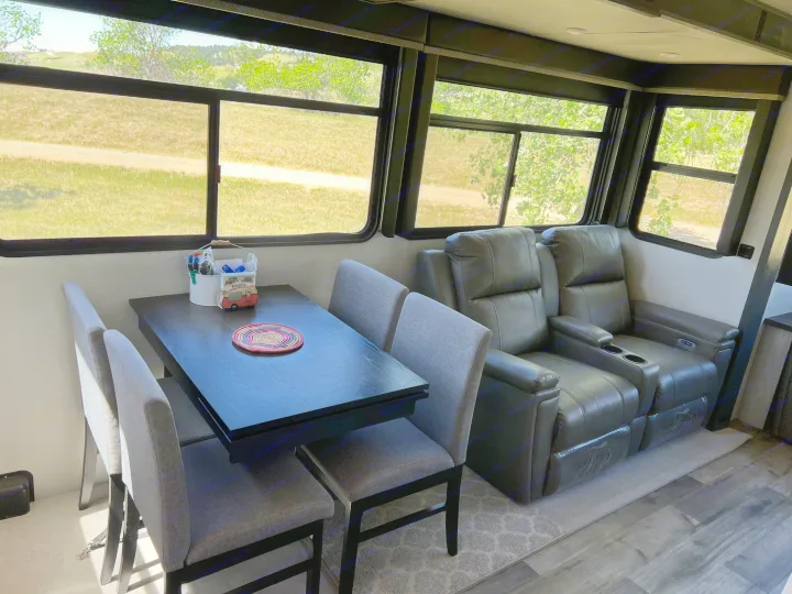 Cozy rv rental interior featuring a dining area with dark table & gray chairs, reclining sofa, and scenic outdoor views.. Keystone RV Montana 2022