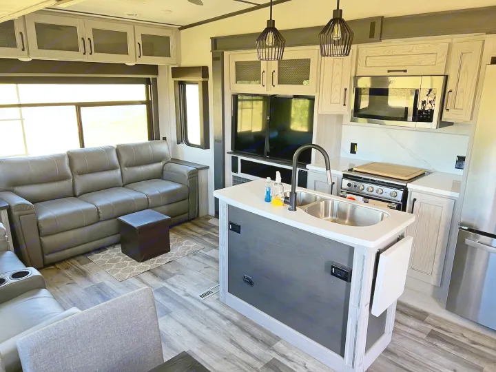 This modern RV rental's interior features a sleek kitchen island, stainless steel appliances, and a comfortable grey sofa in the living area.. Keystone RV Montana 2022