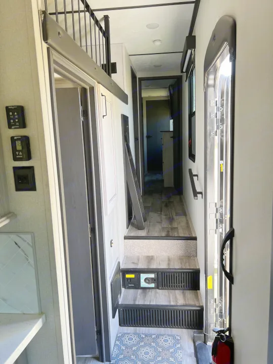 Inside an rv rental: Hallway with stairs, loft railing, control panels, and entry door with fire extinguisher.. Keystone RV Montana 2022