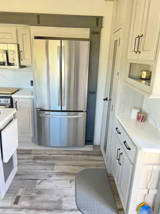 This RV rental has a modern kitchen with a large stainless steel refrigerator, light grey cabinets, and wood-look flooring.. Keystone RV Montana 2022