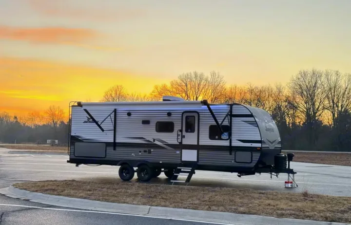Golden sunset lights up this parked RV rental travel trailer. Steps are down, lights on, ready for adventure and travel.. Jayco Jay Flight 2024