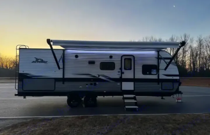 Jay Flight rv rental travel trailer parked with illuminated awning extended, ready for a cozy evening, under a crescent moon sky.. Jayco Jay Flight 2024