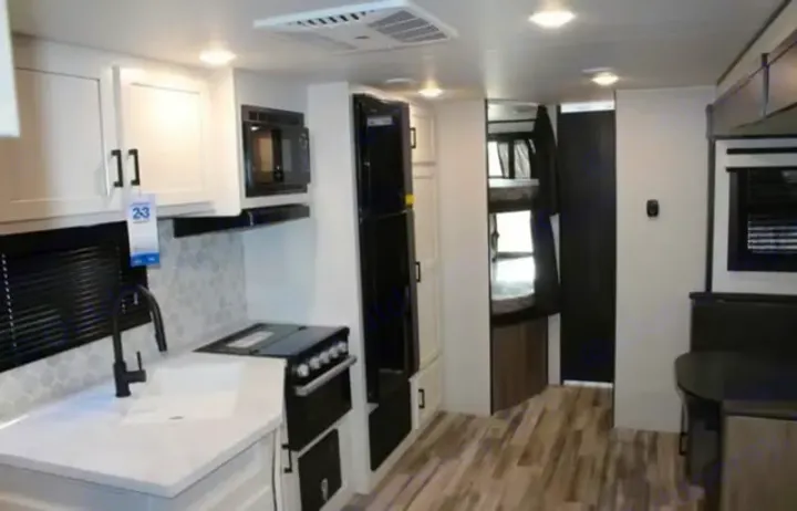 Bright RV rental interior. Features a full kitchen with white cabinets & dark appliances, bunk beds, and a dining area.. Jayco Jay Flight 2024