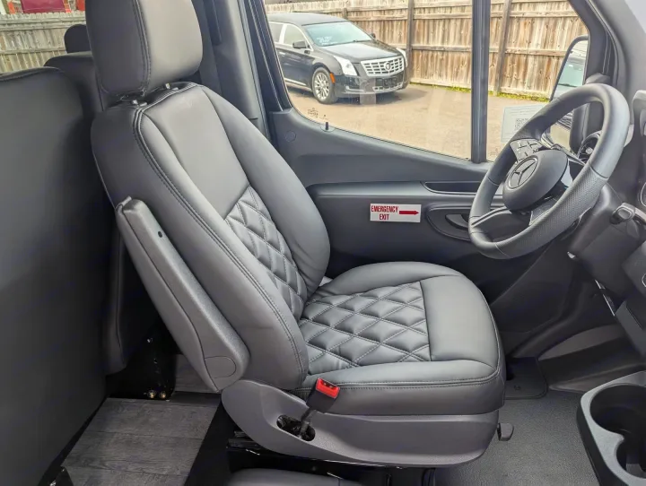 RV rental's gray leather front passenger seat with diamond stitching, Mercedes-Benz wheel, and an emergency exit sign.. Forest River 2025