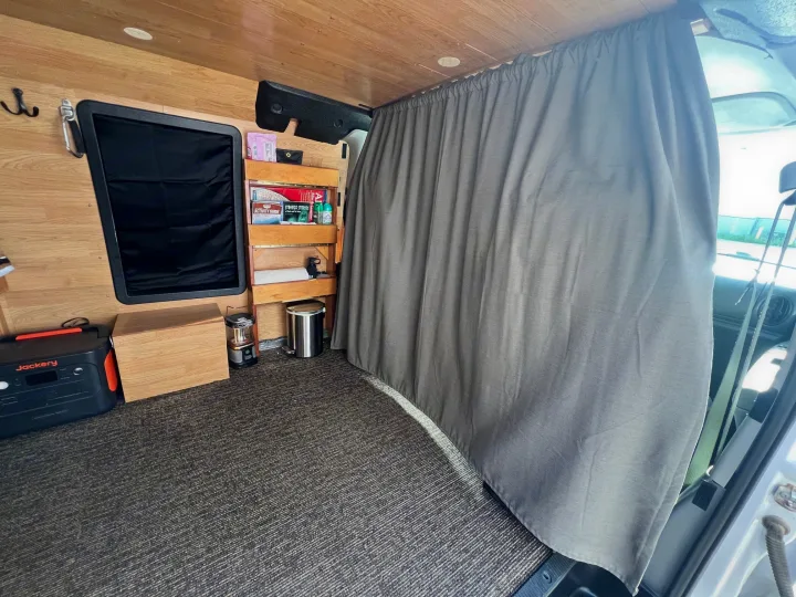 This cozy rv rental interior features wood walls, a privacy curtain, Jackery power station, shelving, and carpet flooring.. Ford Econolline 250s 2006