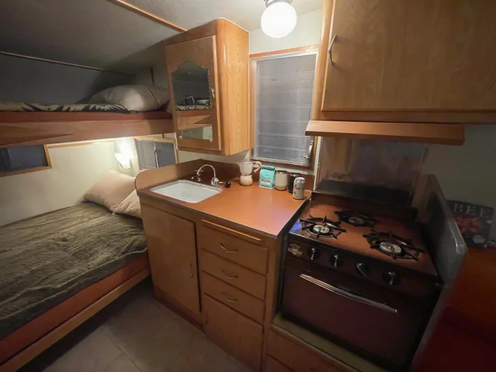 RV rental with cozy bunk beds and a compact kitchen, featuring a sink and vintage-style stove.. Shasta Airflyte 1958