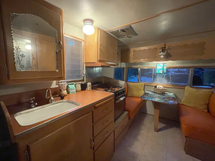 Vintage RV rental: A compact kitchen and cozy dinette with warm wood, stove, sink, and scenic windows for your travels.. Shasta Airflyte 1958