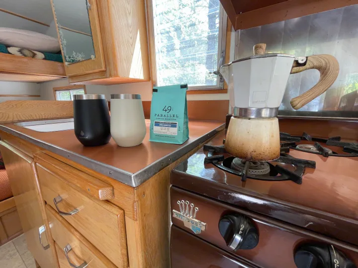 RV rental kitchen with fresh espresso brewing on a Princess stove, 49th Parallel coffee, and Manna tumblers.. Shasta Airflyte 1958