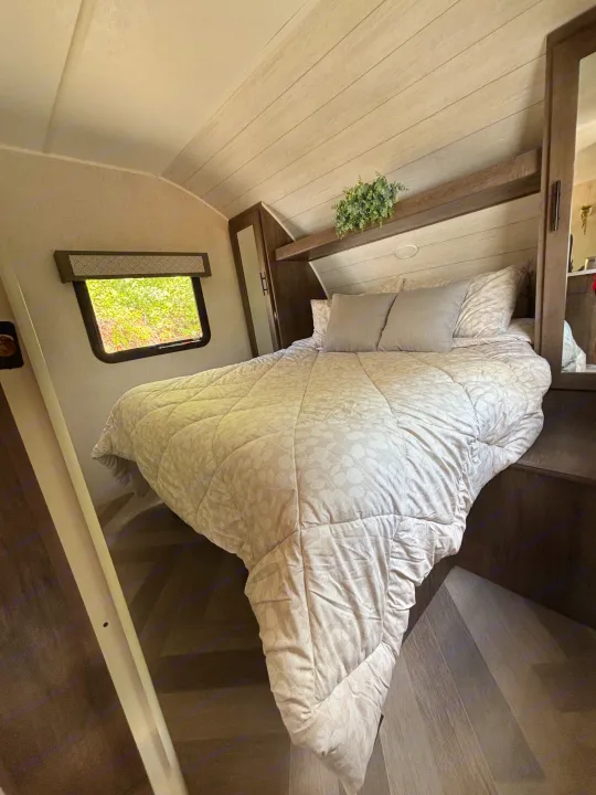 Cozy RV rental bedroom interior, featuring a comfortable bed with patterned comforter, window, and decorative plant.. Forest River Wildwood 2020