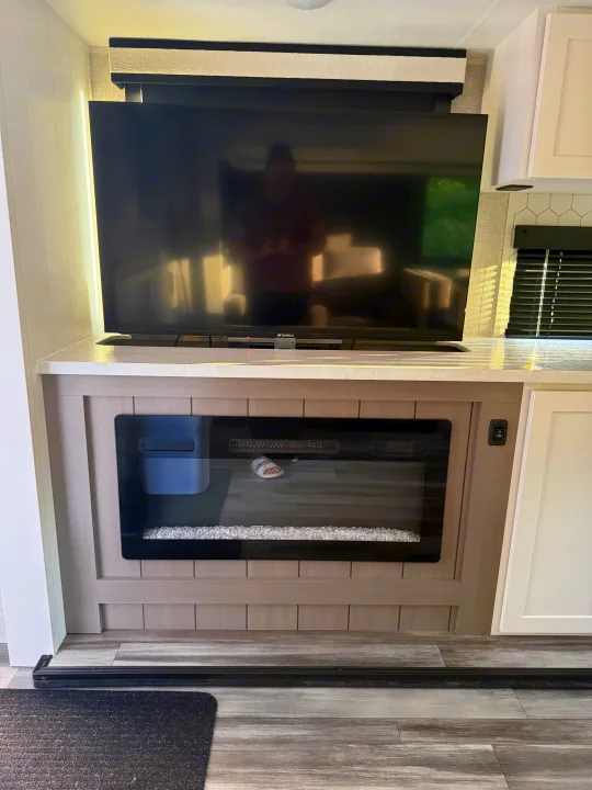 RV rental interior: TV over an electric fireplace on a counter, with modern wood-look flooring. A cozy living space.. Jayco Eagle HT 2025