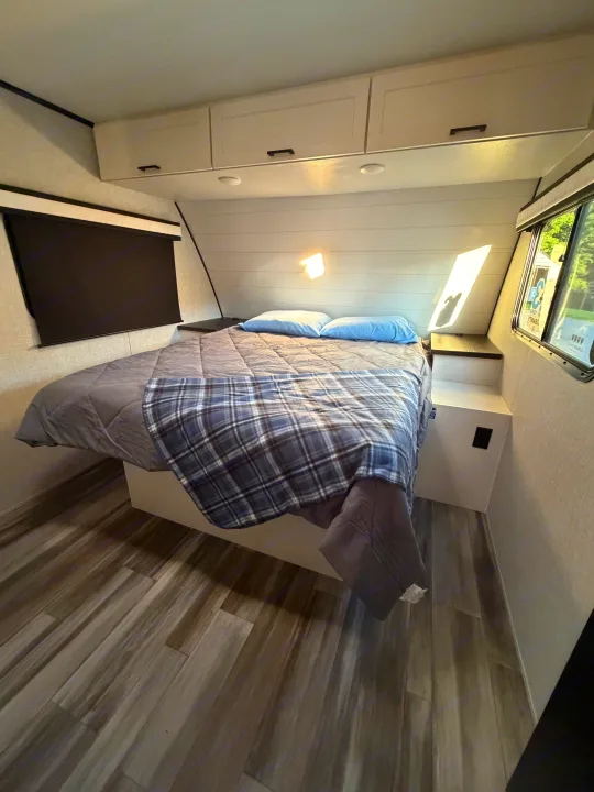 RV rental bedroom: a clean, modern space with a comfy bed, overhead cabinets, wood-look floor, and window views.. Jayco Eagle HT 2025