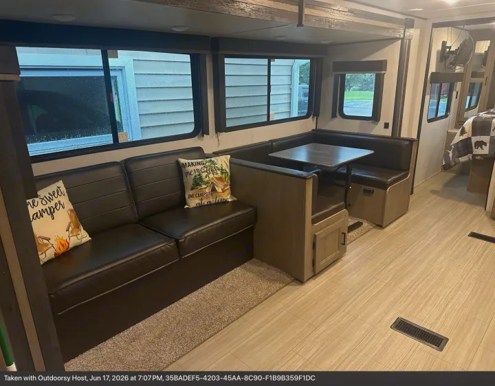 Cozy RV rental interior featuring a black sofa, dinette, light wood-look flooring, and scenic windows.. Keystone RV Hideout Luxury 2021