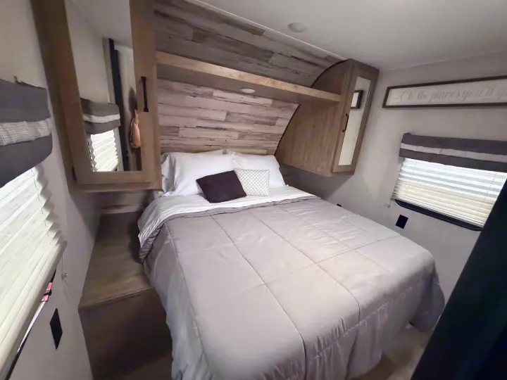 Cozy RV rental bedroom with a queen bed, grey comforter, wood headboard, and built-in mirrored cabinets for a comfortable stay.. Forest River Palomino Puma XLE Lite 2021