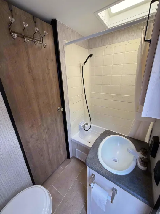 Compact RV rental bathroom showcasing a shower, sink vanity, toilet, and a convenient coat rack on the door.. Forest River Palomino Puma XLE Lite 2021