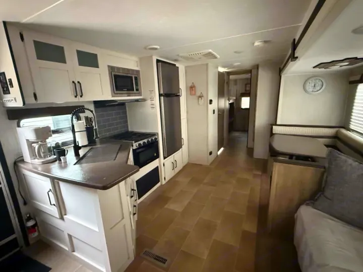 Inside a spacious rv rental: a modern kitchen with white cabinets, stainless appliances, and a cozy dining nook.. Forest River Palomino Puma XLE Lite 2021