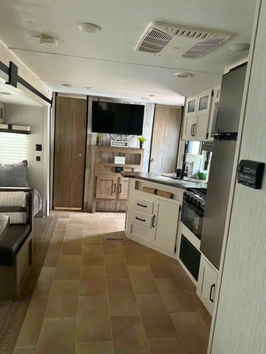 Inside a modern RV rental: a bright kitchen with white cabinets, stove, fridge, and adjacent cozy living/dining area.. Forest River Palomino Puma XLE Lite 2021