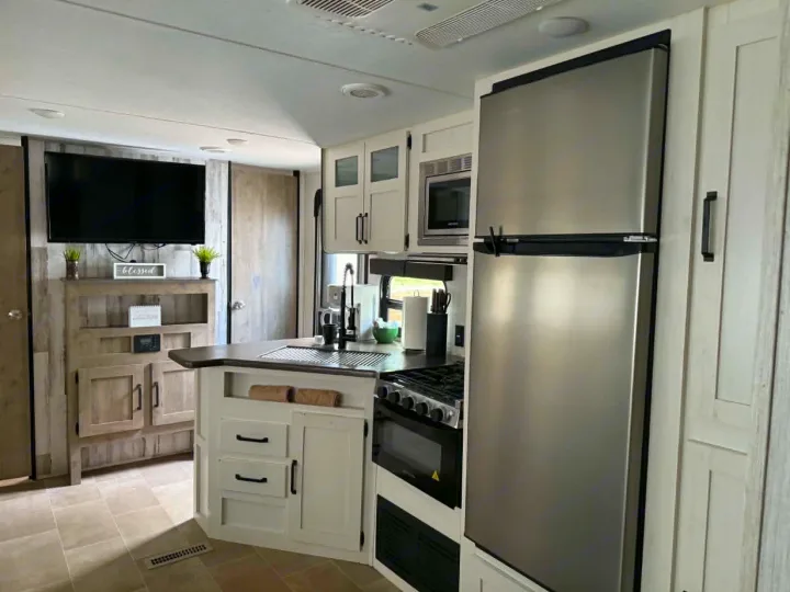 This RV rental showcases a bright, modern kitchen with stainless steel appliances and a comfortable living area with a TV.. Forest River Palomino Puma XLE Lite 2021