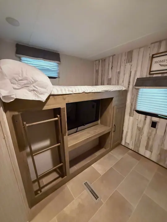Cozy RV rental bunk room with integrated TV, ladder for upper bunk, and rustic wood-paneled walls.. Forest River Palomino Puma XLE Lite 2021