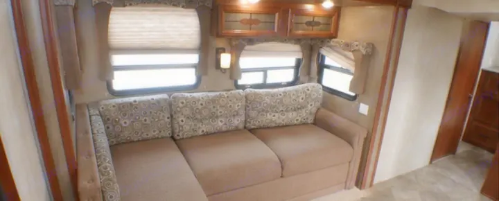 Cozy RV rental living area featuring an L-shaped sofa, large windows with blinds, and overhead cabinets.. Palomino Puma 2015