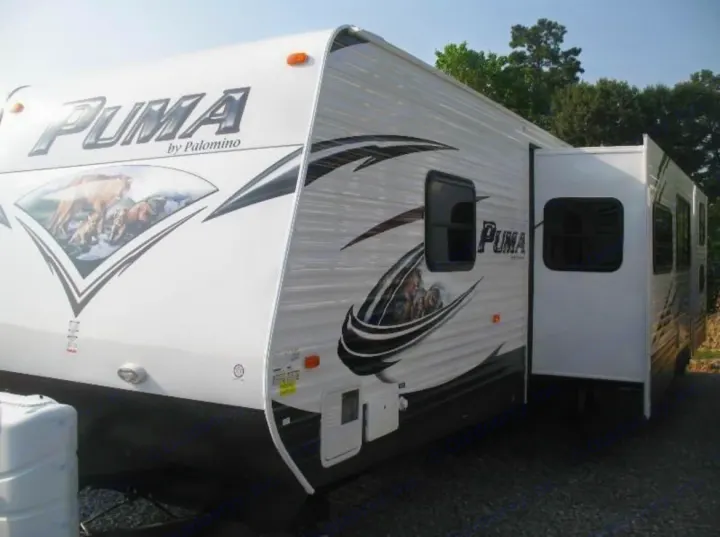 White PUMA by Palomino travel trailer, featuring a slide-out and distinct graphics, ready for your next rv rental.. Palomino Puma 2015