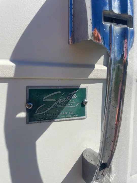 Vintage Shasta RV rental featuring its classic brand emblem and chrome grab handle on a white exterior.. Shasta Airflyte 1958