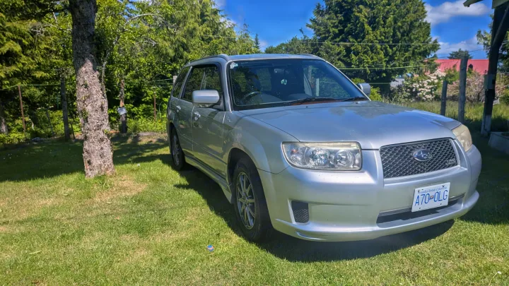 Not an RV rental, this silver Subaru Forester SUV is parked on grass with trees under a sunny sky.. Subaru Forester 2009