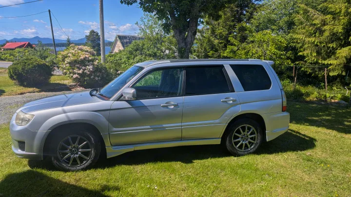 Silver SUV on a sunny lawn, offering scenic lake and mountain views. A perfect vehicle for your next outdoor or RV rental trip.. Subaru Forester 2009