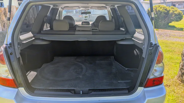 Spacious, open cargo area of a silver SUV. Features upright rear seats, retractable cover. Perfect for your rv rental trip.. Subaru Forester 2009