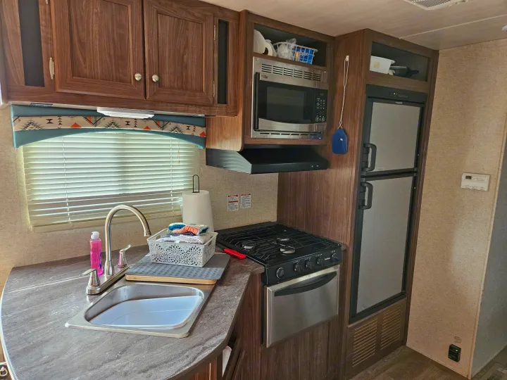 Compact rv rental kitchen: wood cabinets, sink, stove, microwave, and refrigerator. Fully equipped for on-the-road adventures.. Heartland RVs Prowler 2018