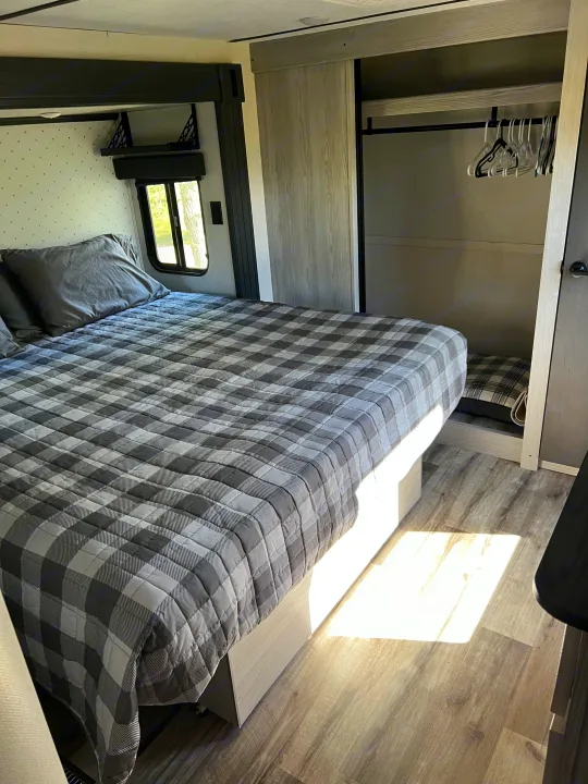 Inviting rv rental bedroom with a comfy plaid bed, window, spacious closet, and sunny wood-look floor.. Keystone RV Montana 2022