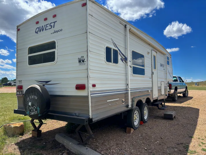 This Jayco QWEST travel trailer, a potential rv rental, is parked and leveled at a sunny campsite with its truck.. Jayco Qwest 2003