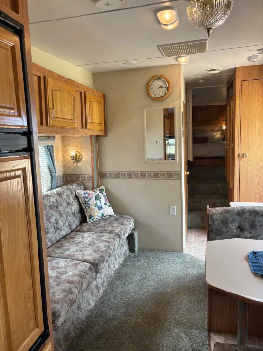 RV rental interior featuring a floral couch, wood cabinets, and steps leading to a private bedroom area.. Jayco Qwest 2003