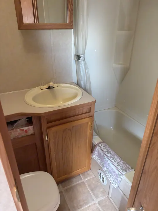 Compact RV rental bathroom with wood vanity, sink, toilet, and shower/tub combo, offering a functional space.. Jayco Qwest 2003