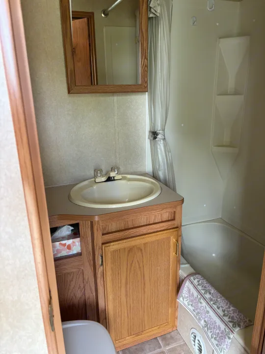 RV rental bathroom: wood vanity with sink, mirror, shower/tub combo, and toilet visible on tile floor.. Jayco Qwest 2003